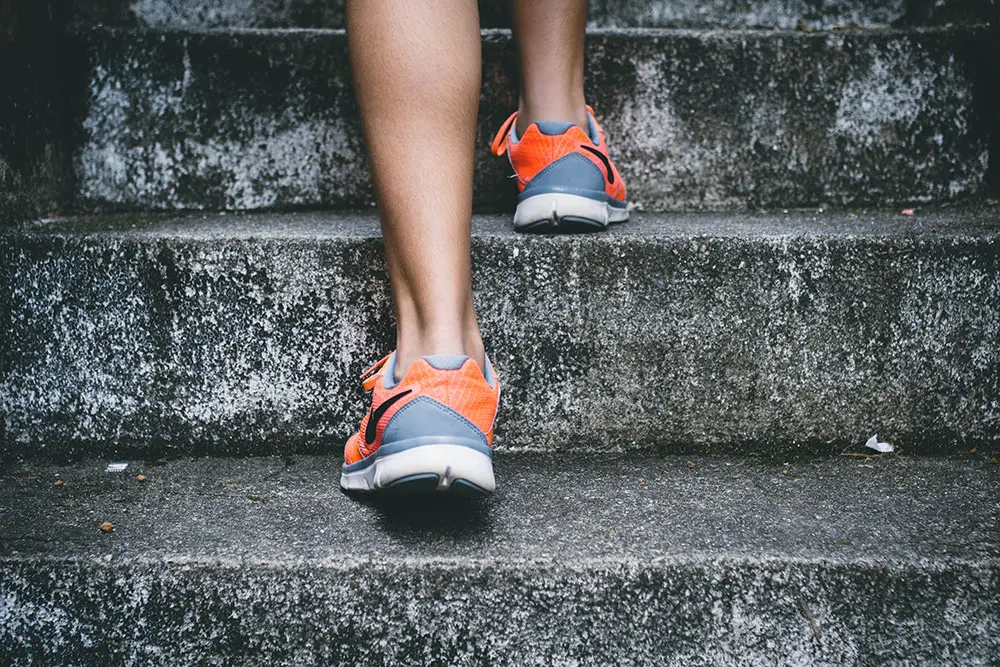 Image showing a mans legs from shin down going up cement stairs wearing white, grey and orange sneakers