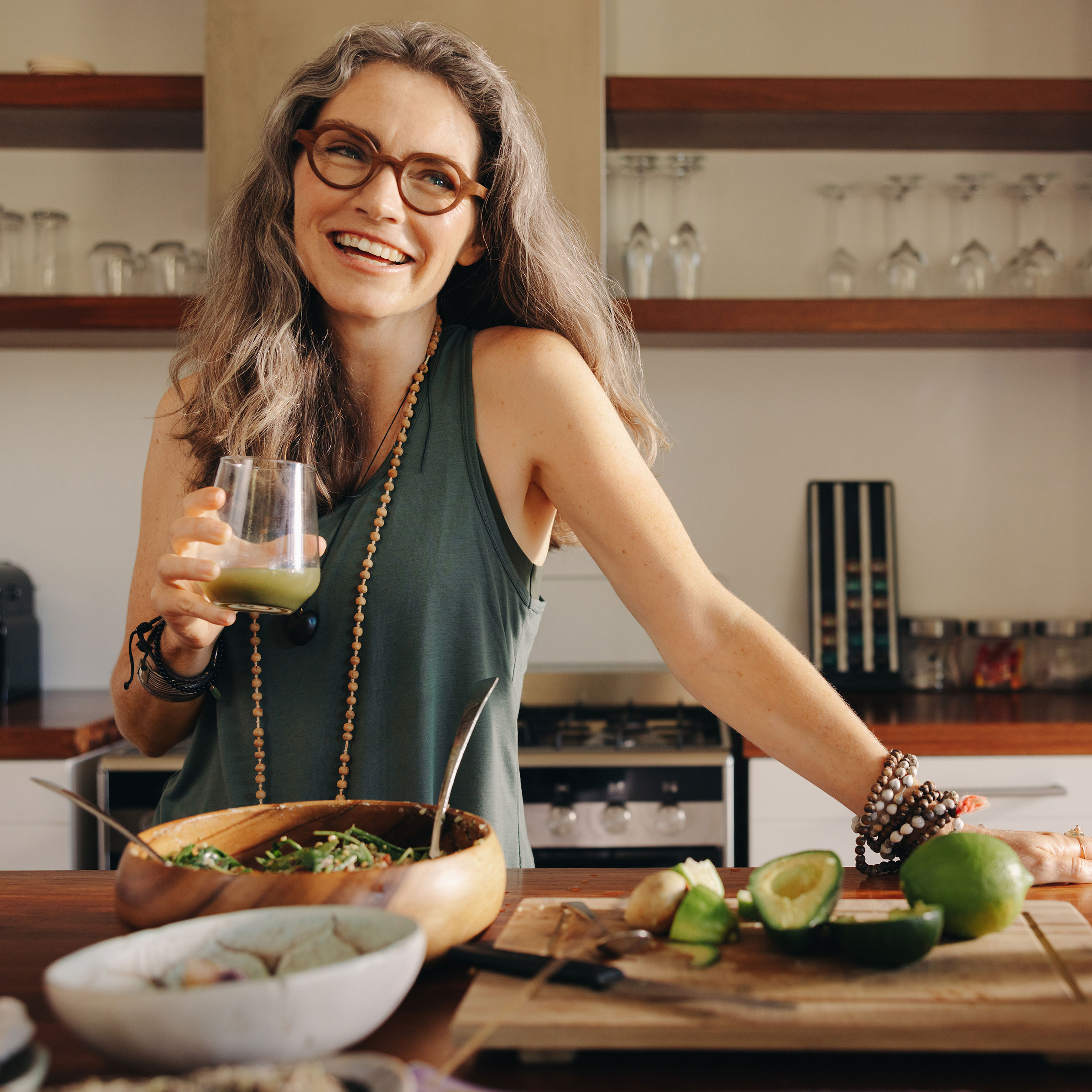 Healthy middle aged women with grey hair wearing a green shirt in the kitchen enjoying nourishing food